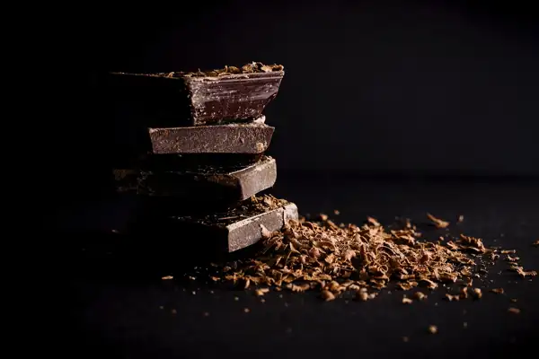 Carrés de chocolat noir empilés et copeaux de chocolat sur fond noir