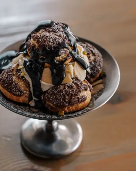 Choux craquelin garnis de crème et nappés de chocolat, sur une coupe en métal
